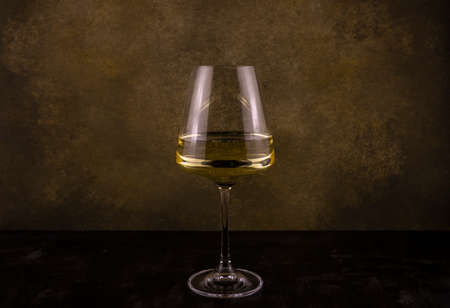 a glass of white wine on a long thin leg on a dark background close-upの写真素材