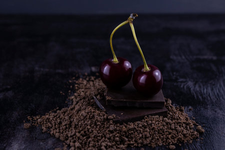 two cherries lying on dark chocolate bars sprinkled with crumbs on a dark background