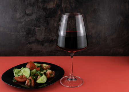 A glass of red wine and a vegetable salad on a red background.の写真素材