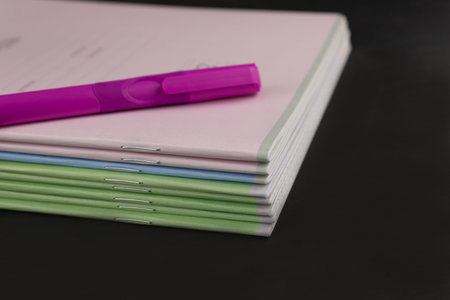 A pink ballpoint pen and a stack of school notebooks on a dark background.の写真素材