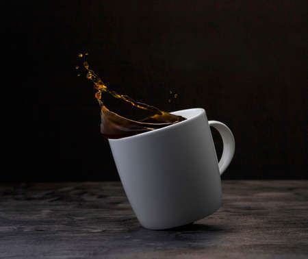 Splashes of black coffee in a white cup on a dark wooden background.の写真素材