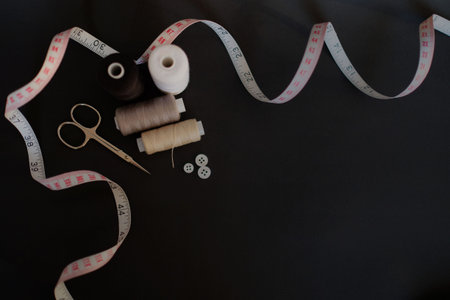 Sewing accessories scissors, measuring tape, thread, buttons on black background with place for...