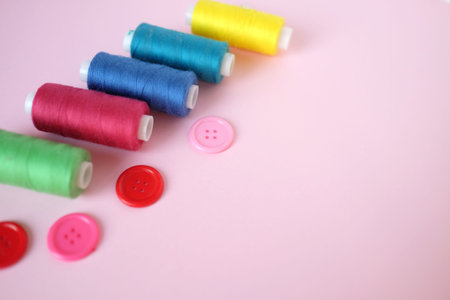 Sewing accessories colorful threads and buttons on pink background with copy space. Flat lay