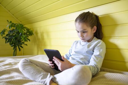 Concept of distance education, free time, technology and internet. Preteen caucasian little student girl with tablet pc at homeの写真素材