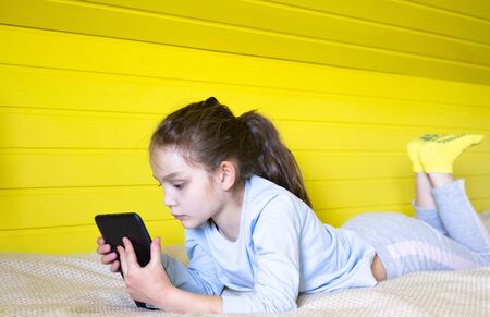 Concept of distance education, free time, technology and internet. Preteen caucasian little student girl with tablet pc at home sitting on couch on yellow backgroundの写真素材