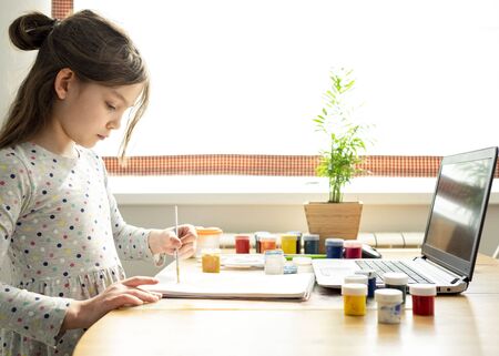 Distance education concept. Covid lockdown. Caucasian girl learns to draw online during self-isolationの写真素材