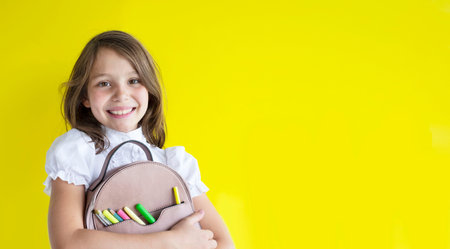 smiling happy schoolgirl. cute caucasian blond girl with backpack with pens, pencils and brushes on...