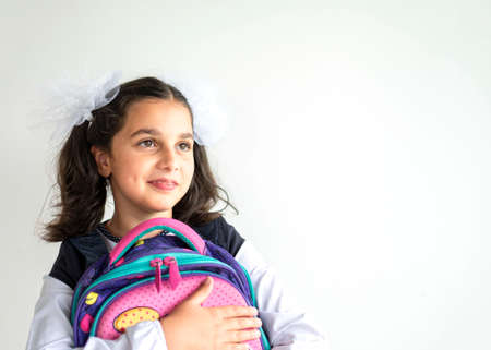 smiling happy schoolgirl. cute caucasian girl with brown hair with two big bows in her hair holds backpack with school supplies on white background. The concept back to schoolの写真素材