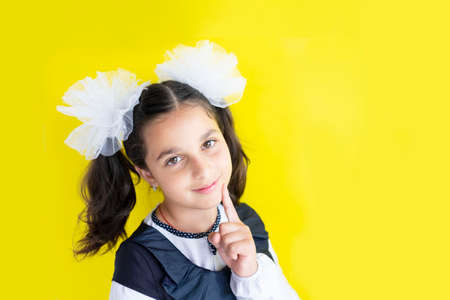 smiling happy dreamy schoolgirl. cute caucasian girl with brown hair with two big bows in her hair gives high five on yellow background. The concept back to school. Copy spaceの写真素材