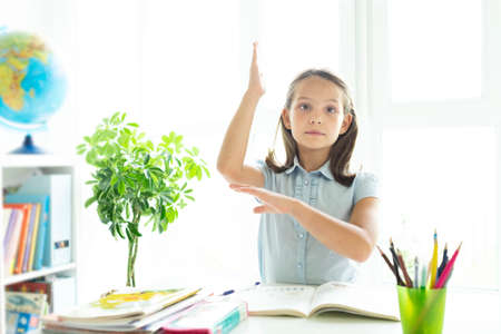 Smiling caucasian girl sitting at desk in class room and looking at workbook. Portrait of young schoolgirl studying at school. Pretty smart pupil writing on notebook.の写真素材
