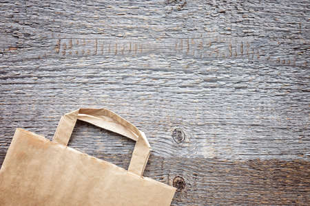 Paper bag on rough wooden board background. Ready-made eco shopping concept. Top view. Flat layの写真素材