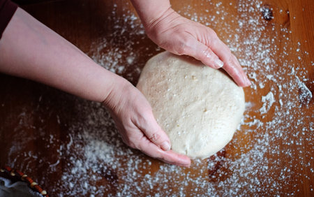 Senior woman hands knead dough on a table in her home kitchen
