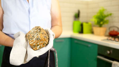 Housewife holds sourdough bread with sunflower and pumpkin seeds in hands in her kitchenの写真素材