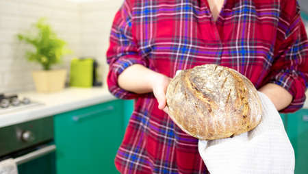 Housewife holds homemade sourdough bread in hands in her kitchenの写真素材