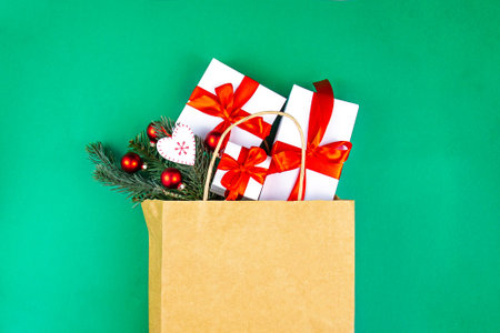 Kraft paper bag on green background. With gift boxes, spruce branches and christmas decoration. Black friday christmas gift preparation concept.の写真素材