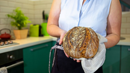 Housewife holds homemade sourdough bread in hands in her kitchen