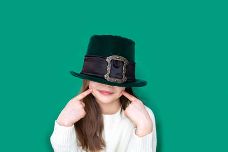 Portrait of cheerful smiling caucasian girl in fancy green leprechaun hat with gold buckle. concept promotion mockup. St. Patricks Day.の写真素材