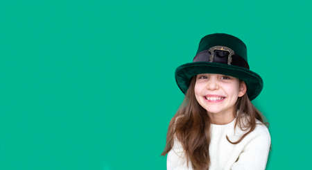 Portrait of cheerful smiling emotional caucasian girl in fancy green leprechaun hat with gold buckle. concept promotion mockup. St. Patricks Day. Banner. Copy spaceの写真素材
