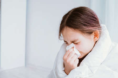 A cold girl blows her nose in a white rag on white background. Rhinitis snot runny nose stuffy nose. Allergy Preteen girl with handkerchief. medical conceptの写真素材