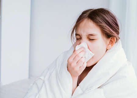 A cold girl blows her nose in a white rag on white background. Rhinitis snot runny nose stuffy nose. Allergy Preteen girl with handkerchief. medical conceptの写真素材