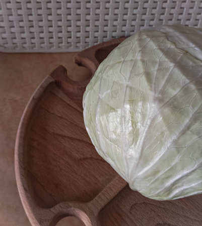 Fresh green cabbage on wooden serving tray in kitchen setting, natural light still life with rustic...