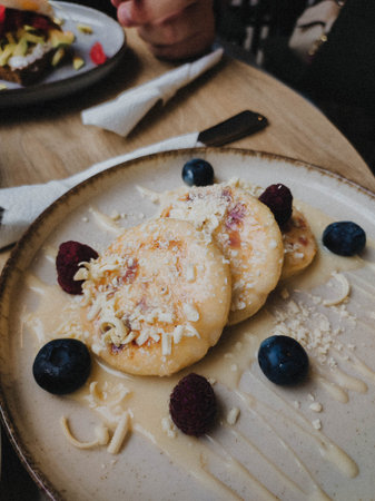 Traditional syrniki served with berries and sweet sauce on ceramic plate. Cozy breakfast scene with...
