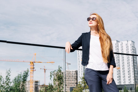 Beautiful business woman in sunglasses and with hair on the background of tall new buildings. Sunny...