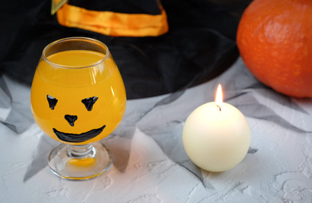 Halloween composition with drink, orange cocktail, pumpkin, candle, hat. Selective focus