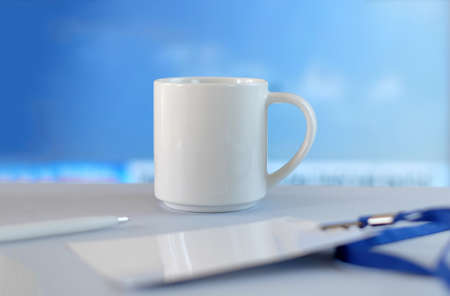 White cup, badge and pen on white table, soft blue backgroundの写真素材