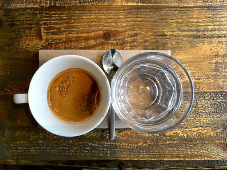 White coffee cup and glass water and spoon on wooden table. Top view.
