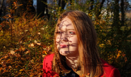 Redhead girl covers her face with shadow of branches, autumn mood concept, nature colorful...
