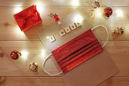 Red medical mask laying on christmas wish list, decoration with lights on wooden background,...
