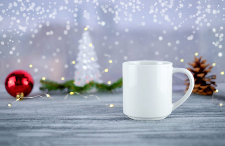 White cup of coffee or tea and Christmas decoration on wooden table near window. Holiday time at...