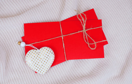 Red envelopes with string and white heart for holidays on the white knitted background, top view.