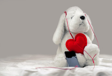 White plush dog toy listening to music on headphones with red heart, copy space