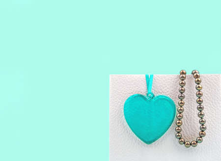 Creative for valentines holiday sale. Turquoise heart and pearl beads on white package on turquoise background, close-up. Copy spaceの写真素材