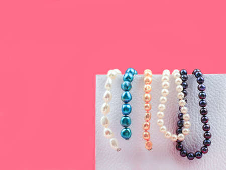Few beads of mix color pearls hanging on a white box on pink background, copy spaceの写真素材