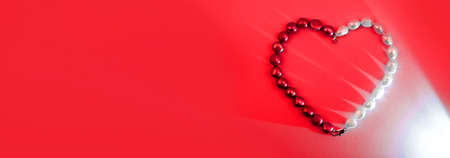 Red and white pearl beads as heart on a red background, banner with copy spaceの写真素材