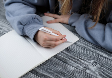 Young girl hand writing the task on copyook on wooden table. Learning at homeの写真素材