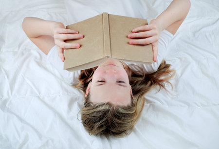 Teenage cute girl with notebook in hands while laying on her back on the bed. Above view