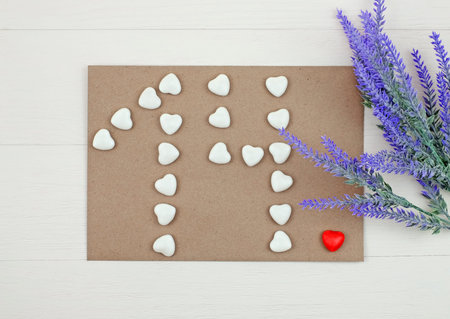 Number 14 formed with hearts candies on envelope and flowers. Top view