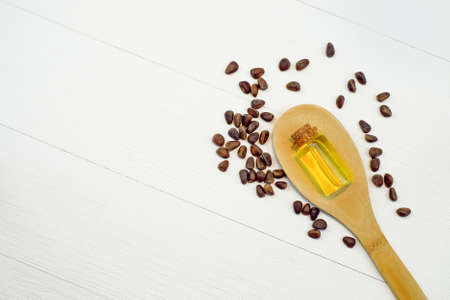 Essential cedar oil in small glass bottle in wooden spoon and nuts on white wooden background. Top view. Copy spaceの写真素材