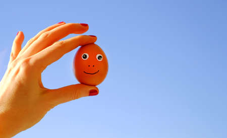 Funny egg with eyes in a hand on blue skysunny background, copy spaceの写真素材