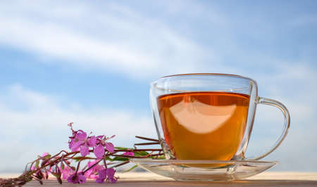 Glass cup of tea with willow-herb on blue sky backgroundの写真素材