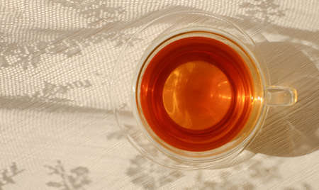 Glass tea cup on wooden background with shadows of openwork curtain, rural style, top viewの写真素材
