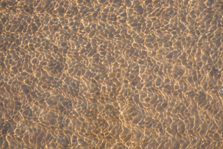 View through the water and waves on the sand with sunlight, abstract natural marine background
