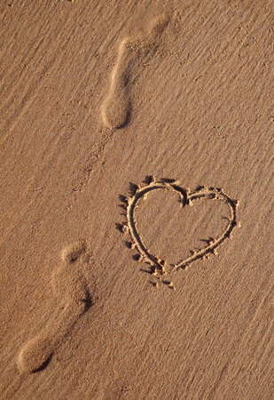 Heart symbol drawn on the beach and sand human footprints, vertical image.