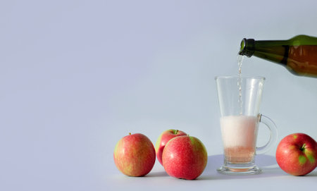 Pouring of rose apple cider in glass and red apples on blue background with copy spaceの写真素材