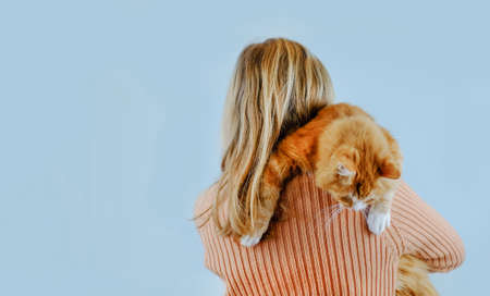 Girl holds her cat on shoulder on blue background. Copy spaceの写真素材