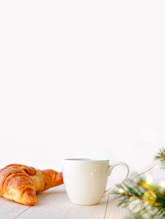 Cup of coffee or tea with croissant and christmas decor on white background, vertical photo with copy spaceの写真素材